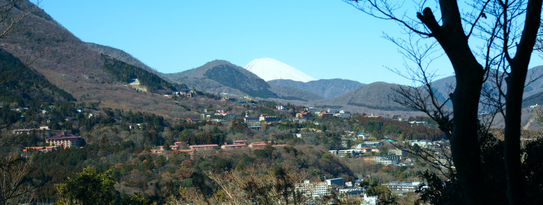 A stunning mountain range landscape featuring towns stretching out against the backdrop of Mt. Fuji.