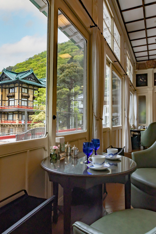 A serene lounge with a view of the 「FLOWER PALACE」 outside the window. On the table, there are cups, glasses, and flowers, creating a relaxing atmosphere